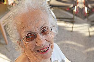 Femme âgée aux cheveux blancs portants des lunettes et souriant.